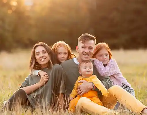 Family of five sitting together in a sunlit field during golden hour.