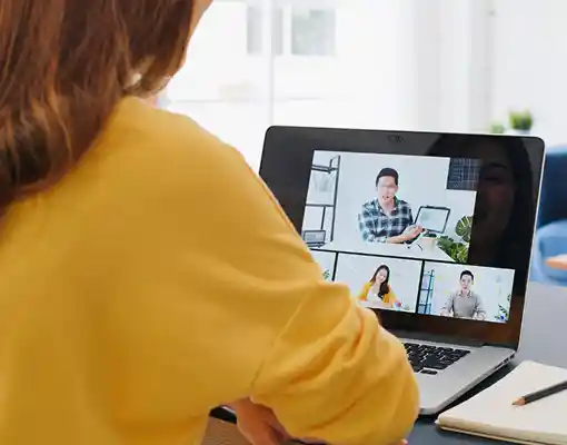 Person in yellow shirt participating in a virtual meeting with three people on a laptop screen.