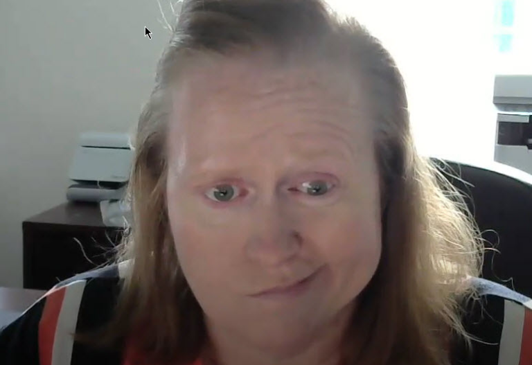 Middle-aged woman with light brown hair, wearing a striped shirt, seated in an office setting.