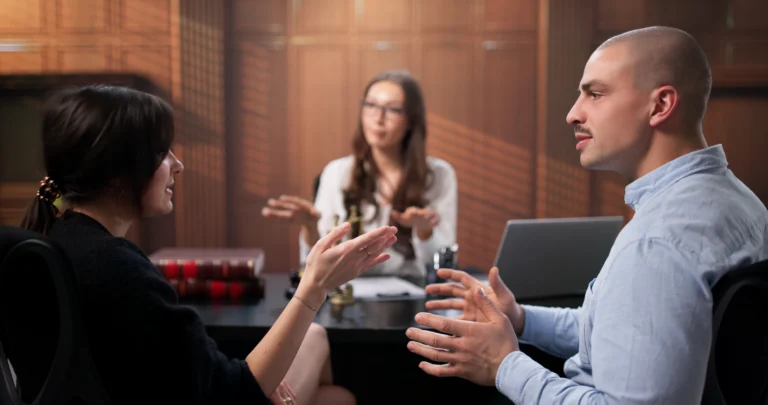 Three professionals engaged in a discussion in a wood-paneled office with books and laptop.