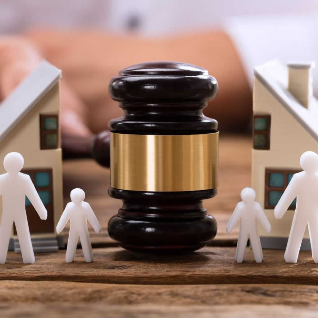 Wooden judge's gavel with gold band between two miniature house models and white family figures.