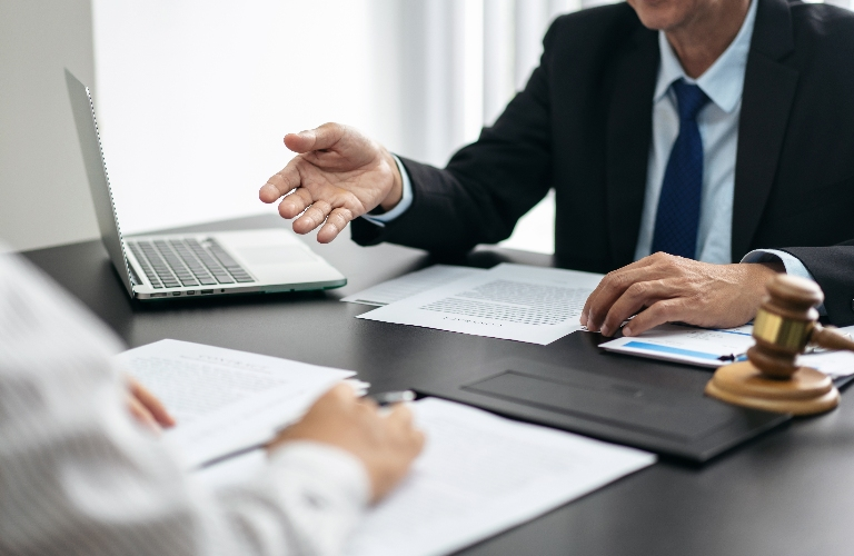 Two professionals discussing documents at a desk with a laptop and a wooden gavel.