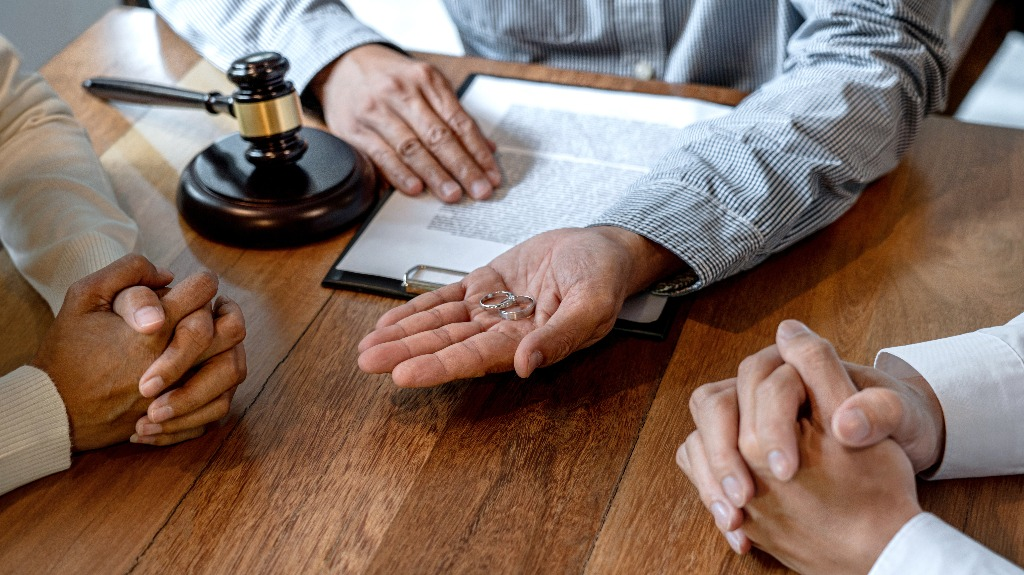 Hands of three people around a wooden table with wedding rings, a gavel, and a legal document.