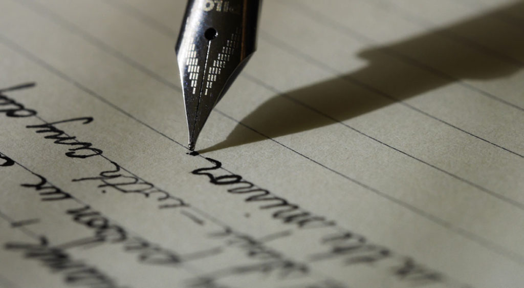 Close-up of a fountain pen writing cursive text on lined paper with shadow.