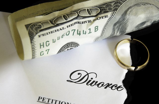 Close-up of a torn divorce petition, a gold wedding ring, and a rolled US hundred-dollar bill.