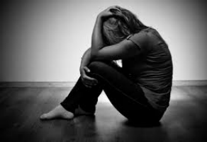 Black and white image of a person sitting on the floor, head in hands, appearing distressed.