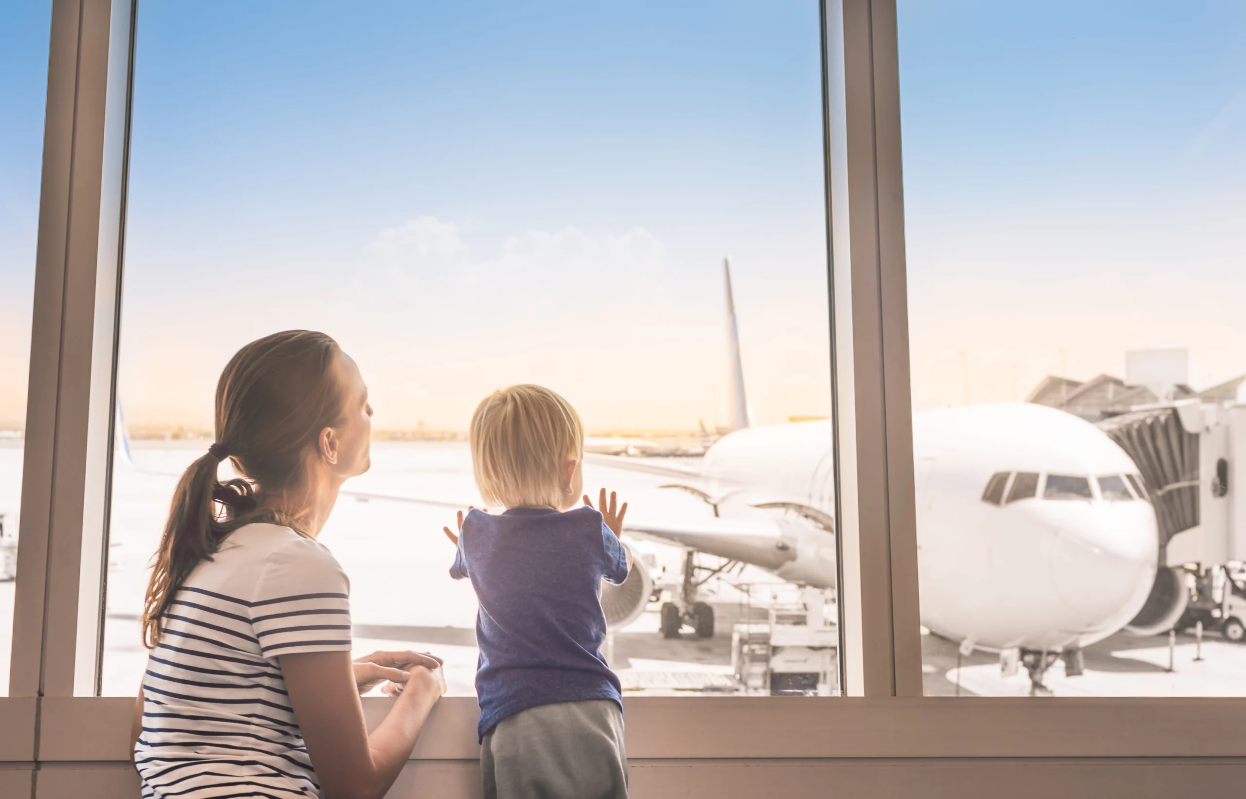 Woman and child looking through large airport window at a parked airplane.