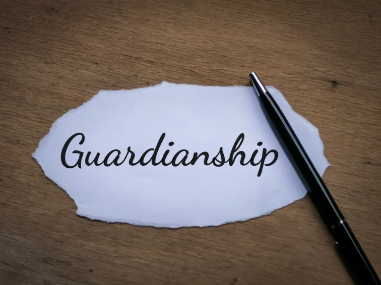 Black pen resting on torn white paper with the word "Guardianship" written in cursive, on a wooden surface.