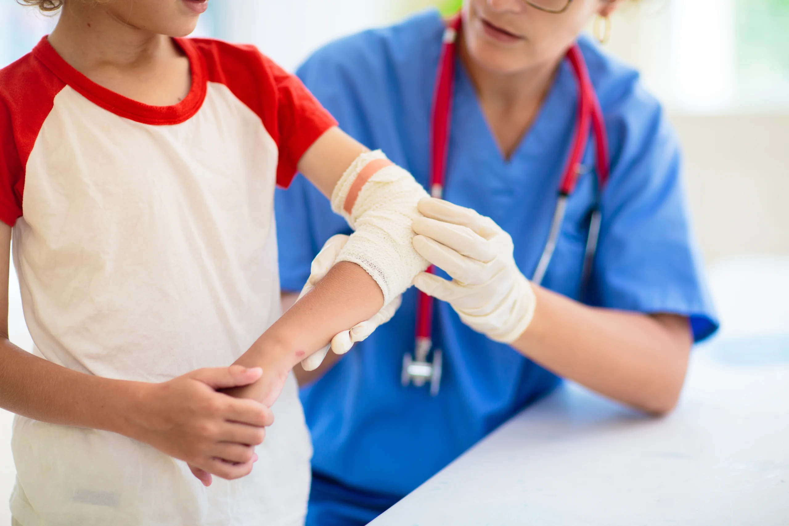 Healthcare professional in blue scrubs bandaging a child's arm injury.