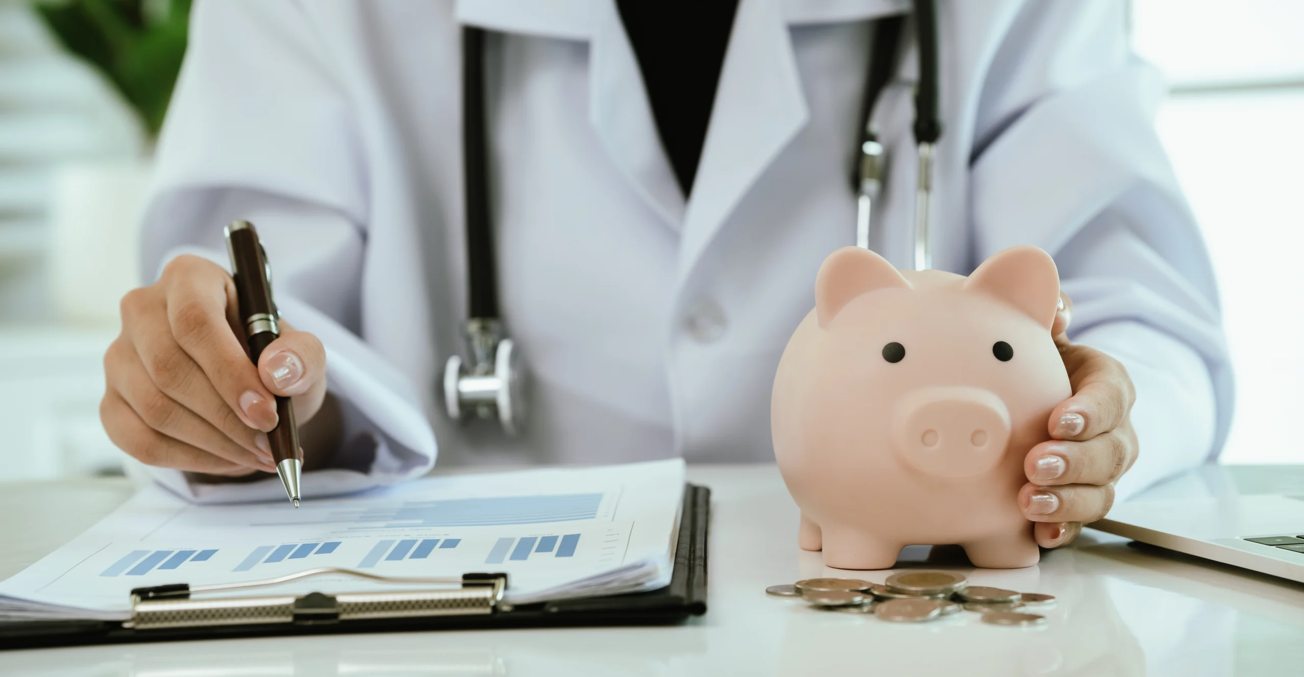 Medical professional in white coat holding piggy bank and pen over financial documents.