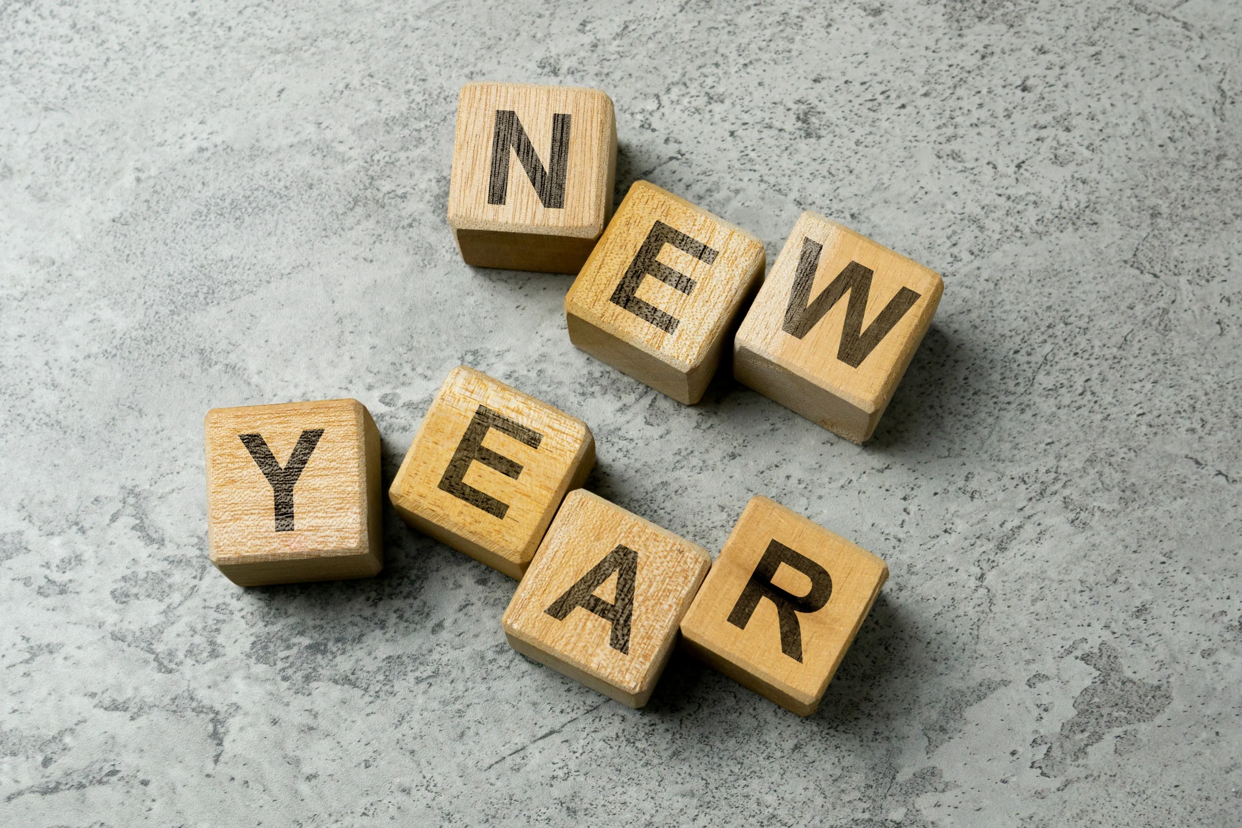Wooden letter blocks on gray textured surface spelling the word "NEW YEAR.