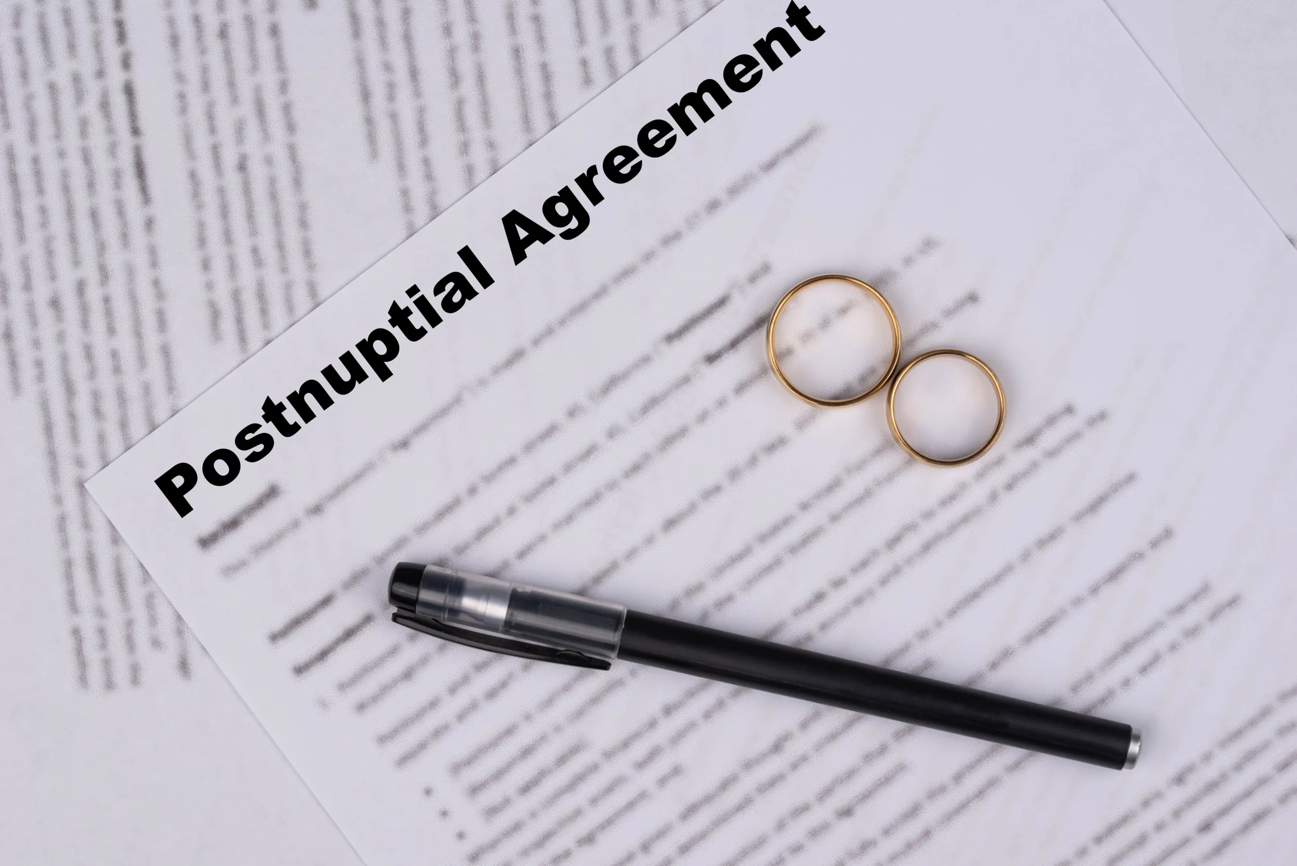 Postnuptial agreement document with two gold wedding rings and a black pen.