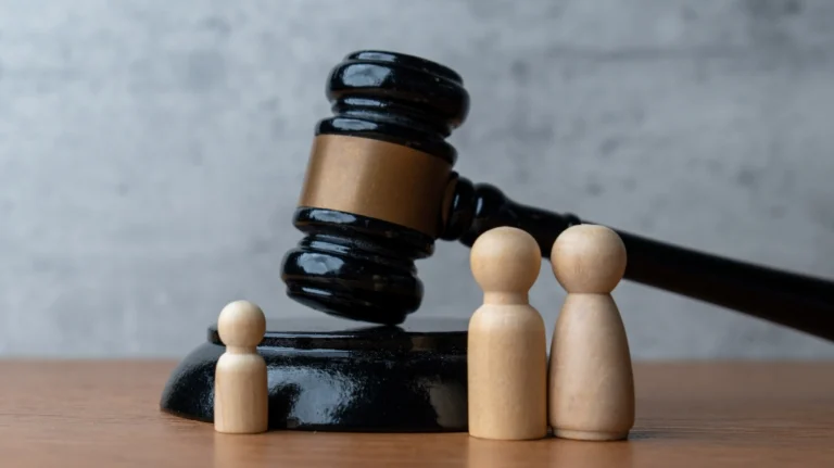 Black judge's gavel resting on sound block with three wooden figurines on wooden surface.