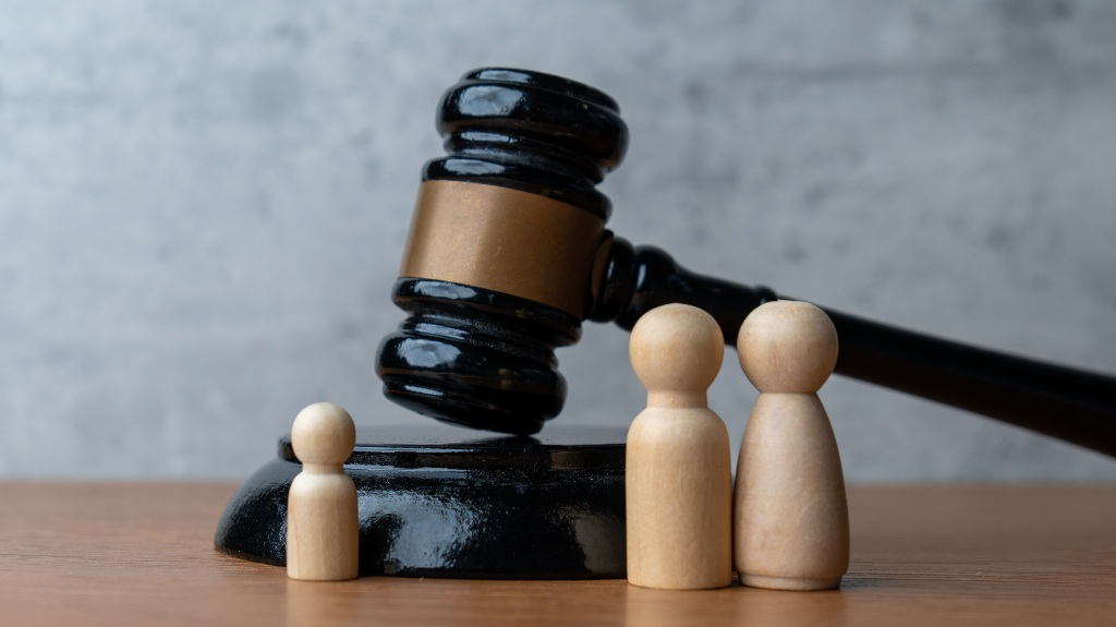Black judge's gavel resting on sound block with three wooden figurines on wooden surface.