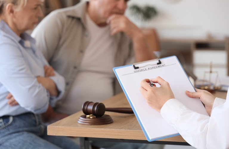 Professional holding a pen and clipboard labeled "Divorce Agreement" with a couple seated nearby.
