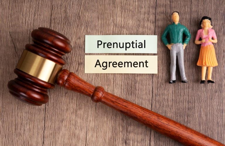 Wooden judge's gavel, "Prenuptial Agreement" text, and male and female figurines on wood surface.