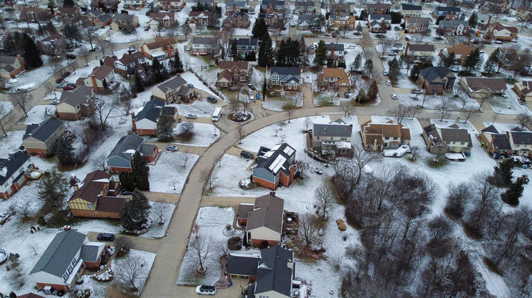 Aerial view of a suburban neighborhood with snow-covered lawns and houses during winter.