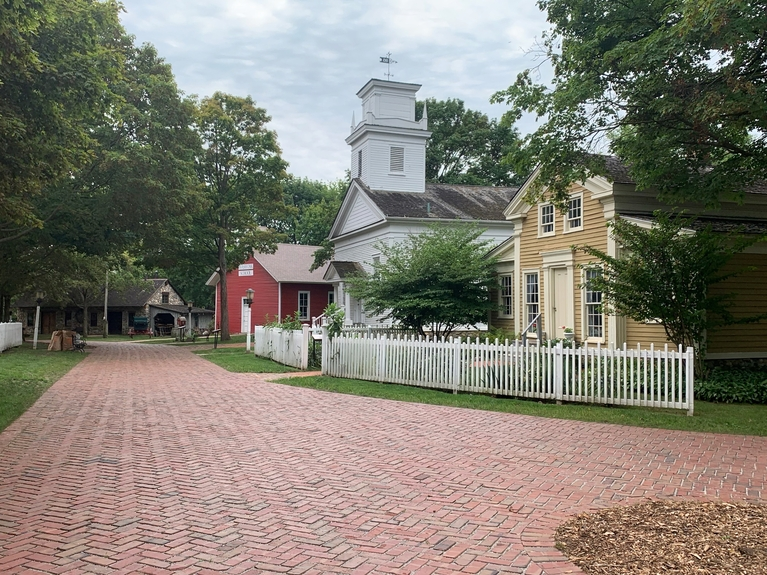 Brick-paved street lined with white picket fences, historic white church, and colorful buildings.
