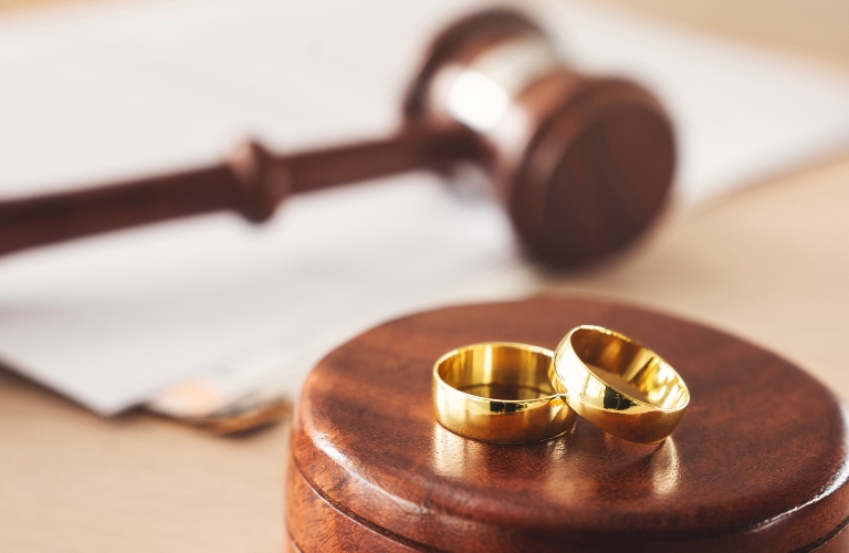 Close-up of two gold wedding rings on a wooden judge's gavel base with a blurred gavel in the background.