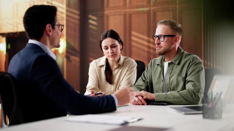 Three professionals engaged in a discussion at a modern office desk with documents and a laptop.