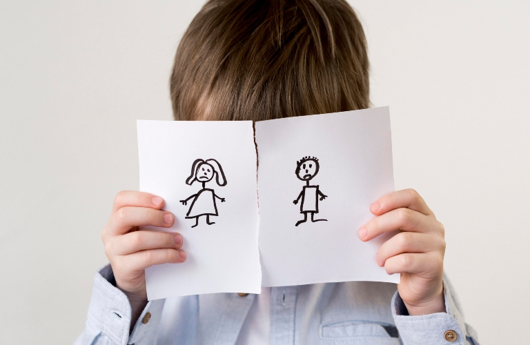 Child holding torn paper with sad stick figure drawings of a girl and boy.