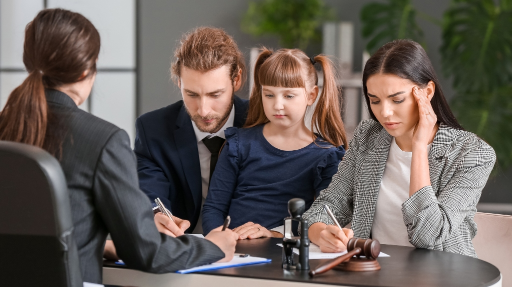 Four individuals at a table: a man, a woman, a young girl, and a professional woman with legal documents and a gavel.