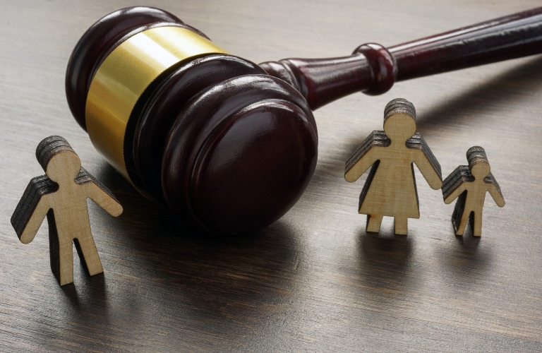 Wooden judge's gavel with gold band placed on a dark wooden surface alongside three wooden family figures.