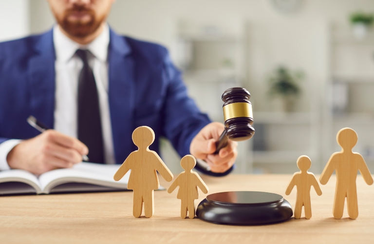 Man in blue suit holding gavel above wooden family figures on desk.