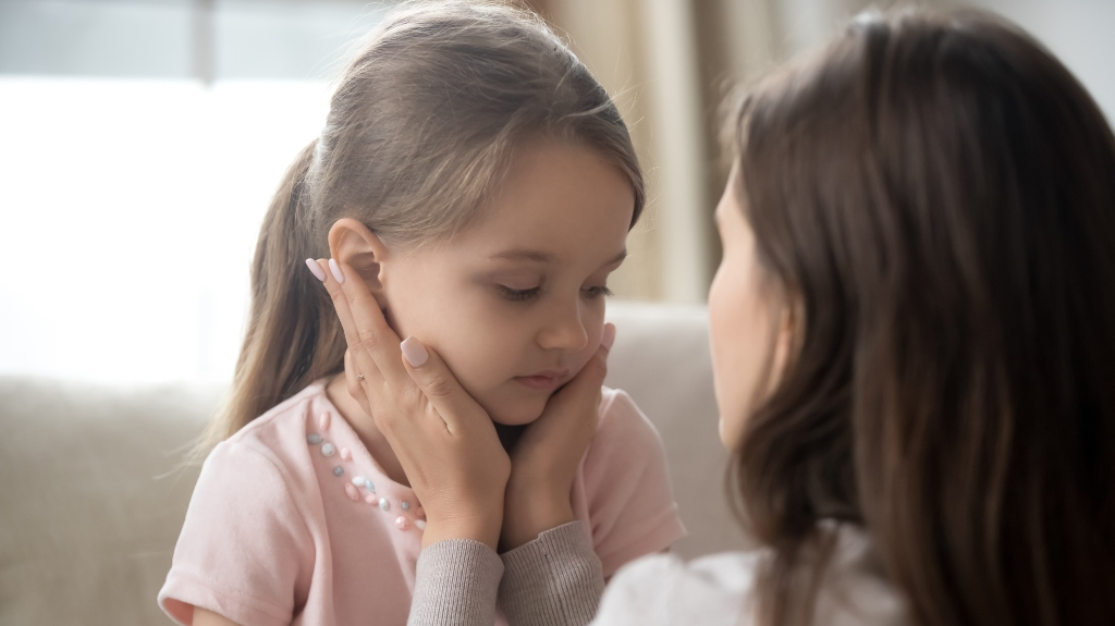 Woman gently holding and comforting a young girl in a pink shirt indoors.